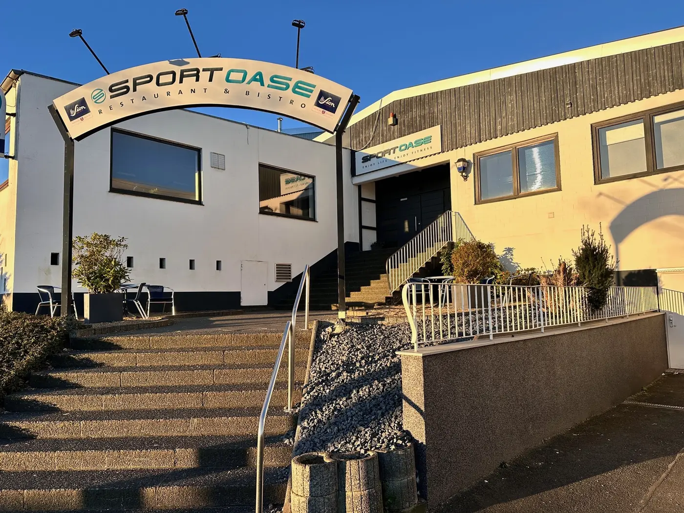 Eingang der Sport Oase in Wesseling mit Schriftzug und Treppe im Abendlicht